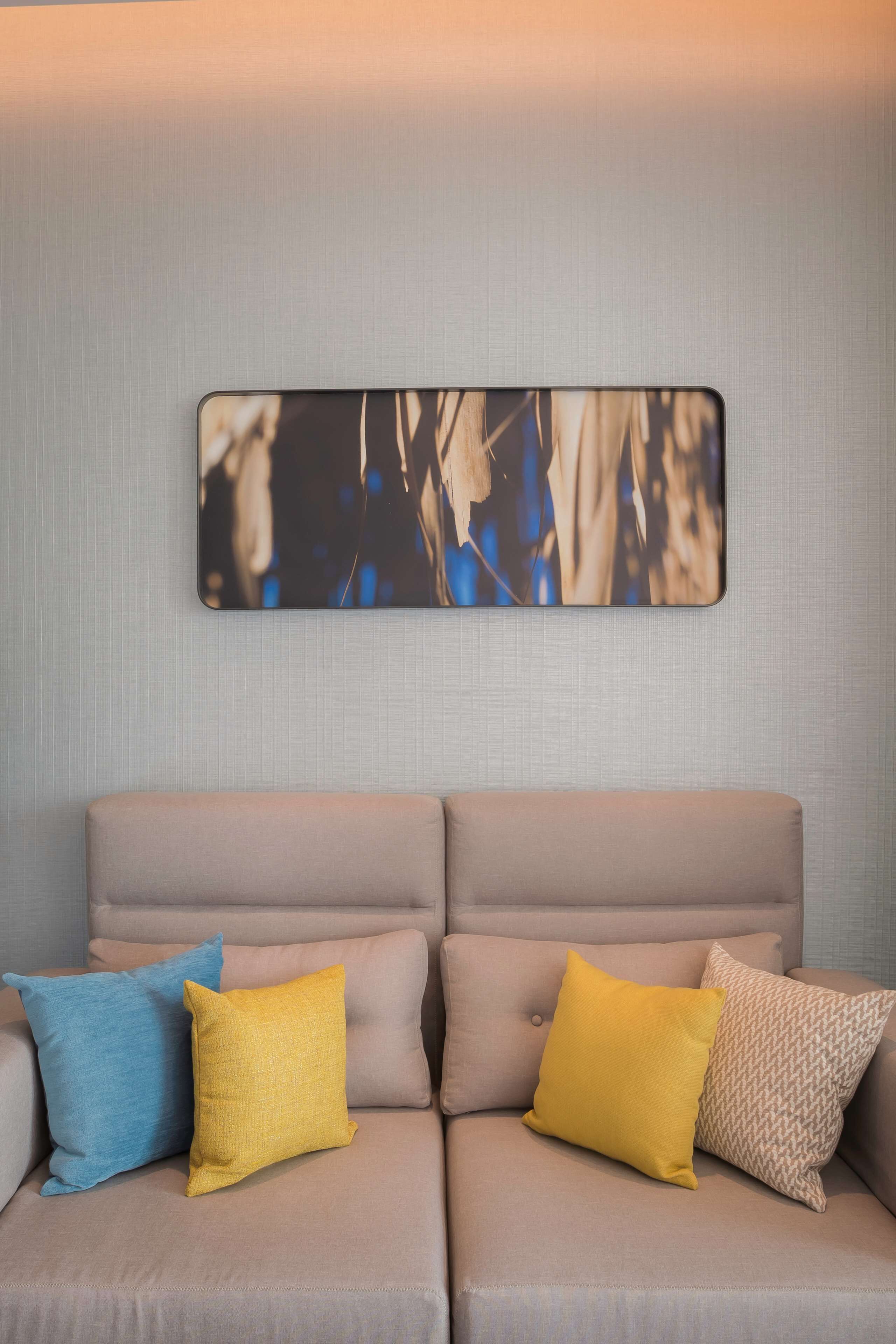 Ein Sofa mit drei Kissen in verschiedenen Farben und einem an der Wand hängenden abstrakten Kunstwerk.