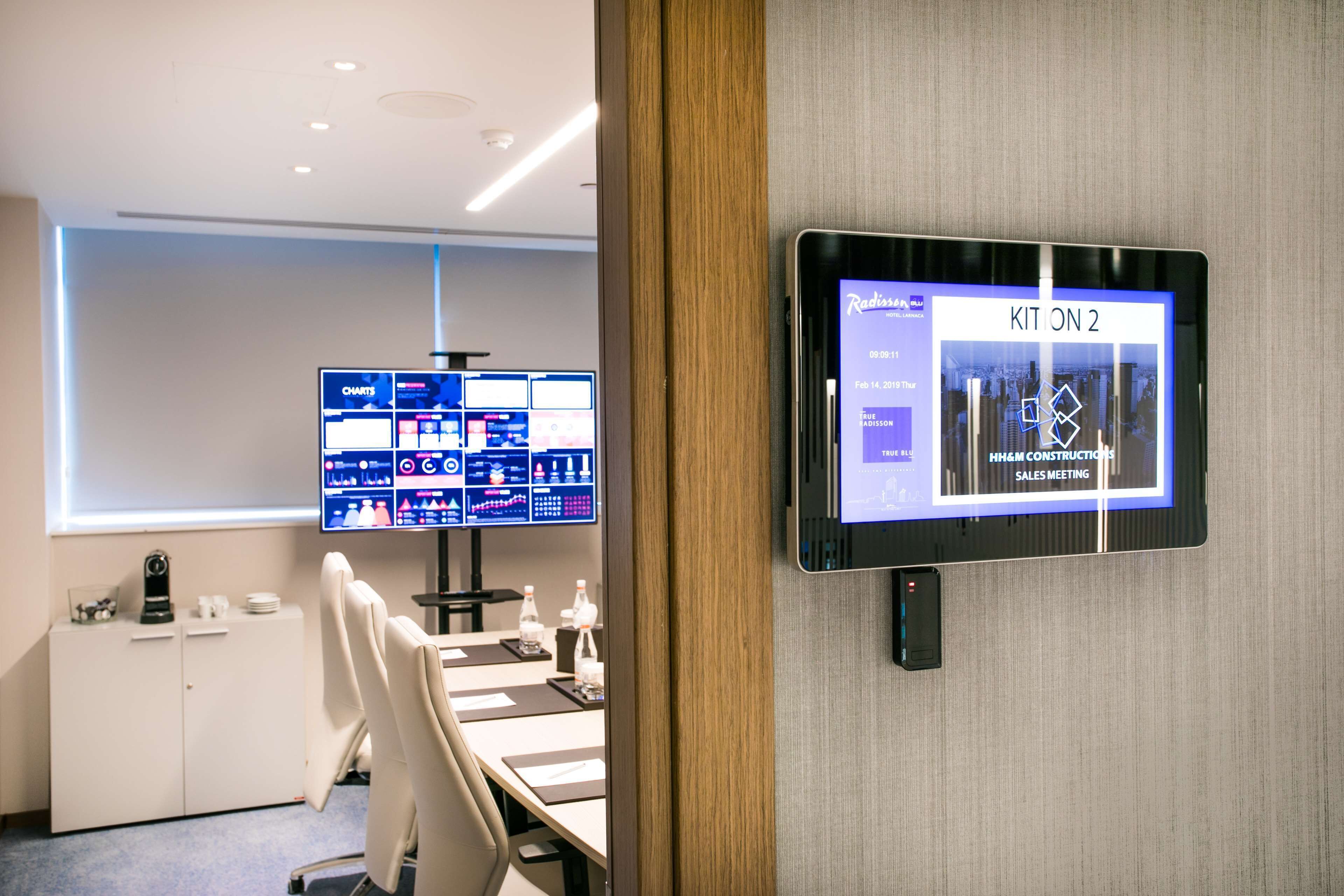 Una sala de conferencias moderna con una gran pantalla digital, una pizarra y un escritorio con una silla.