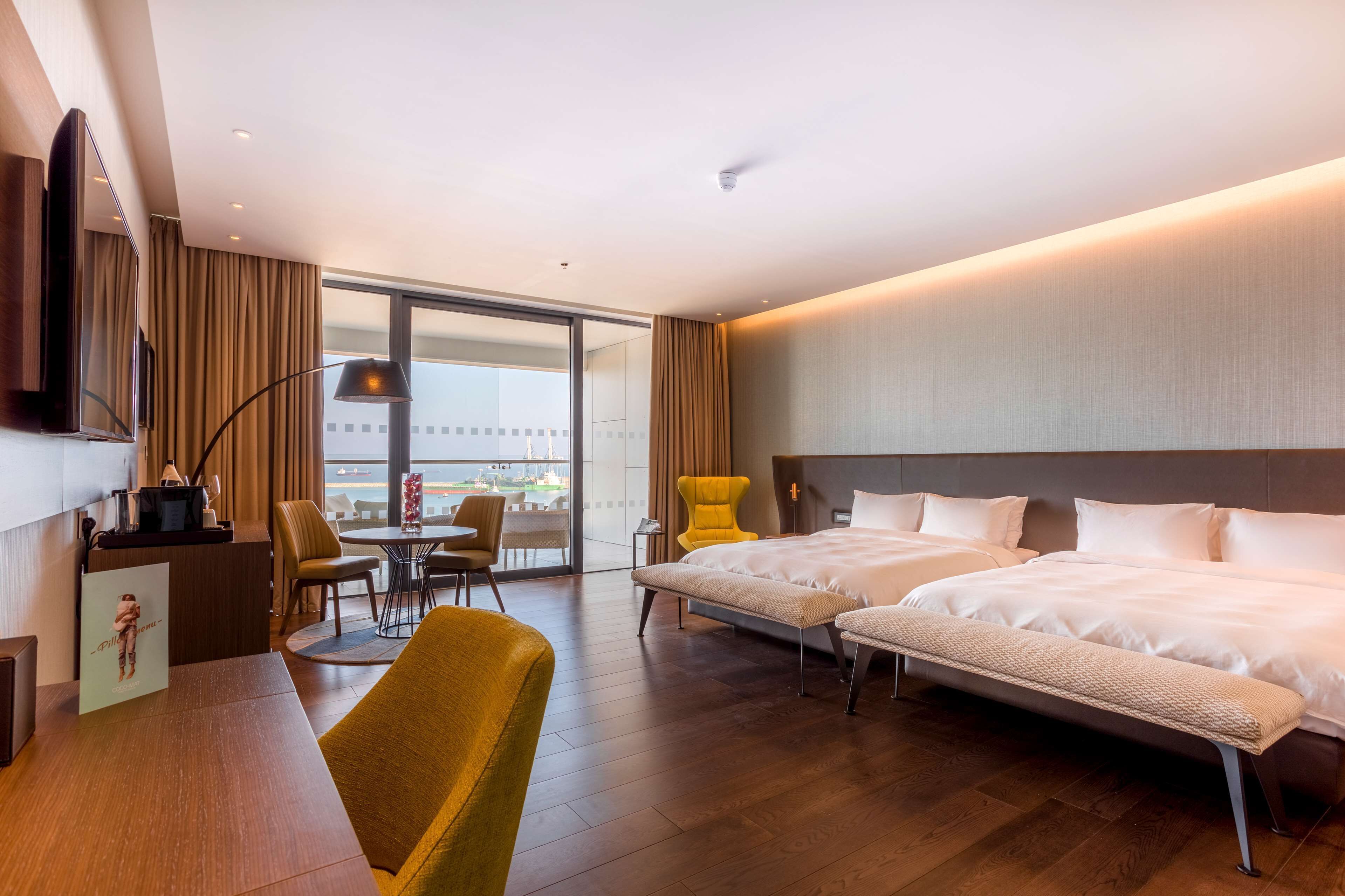 A hotel room with a large bed, a desk, a chair, a television, and a view of the city.