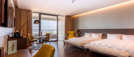 A hotel room with a large bed, a desk, a chair, a television, and a view of the city.