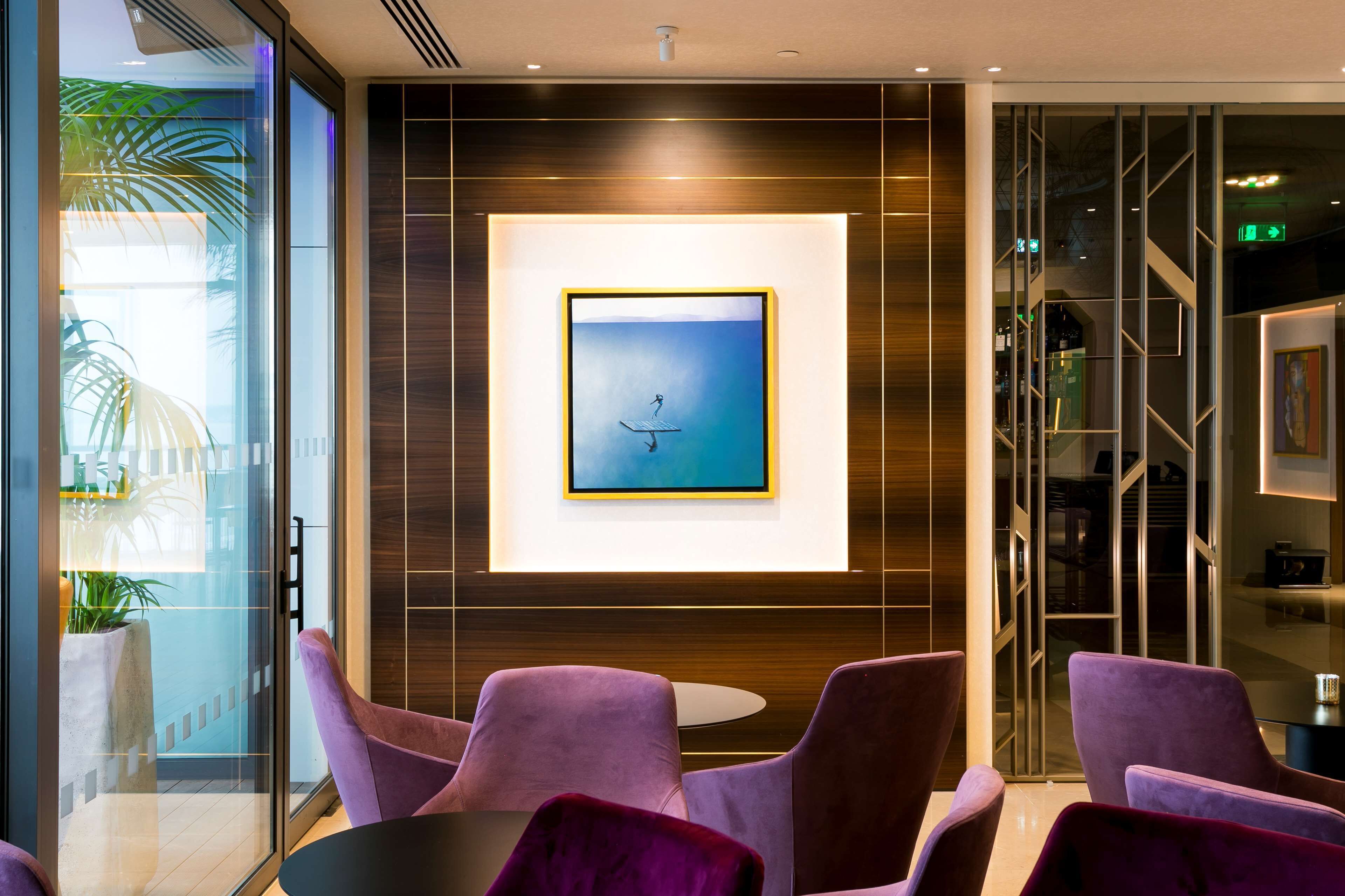 A modern lobby with purple chairs, a framed artwork, and a glass wall with a plant.