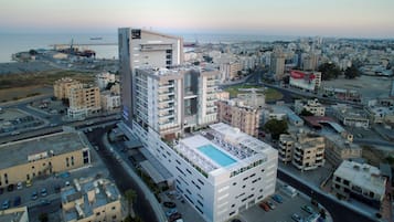 A high-rise hotel with a rooftop pool, multiple floors, and a view of the cityscape and sea.