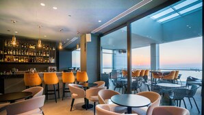 A modern bar area with a large window overlooking a scenic view, featuring a variety of seating arrangements and a well-stocked bar.