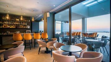 Zona de bar moderna con un amplio ventanal que ofrece vistas panorámicas, con diferentes opciones de asientos y una barra bien surtida.