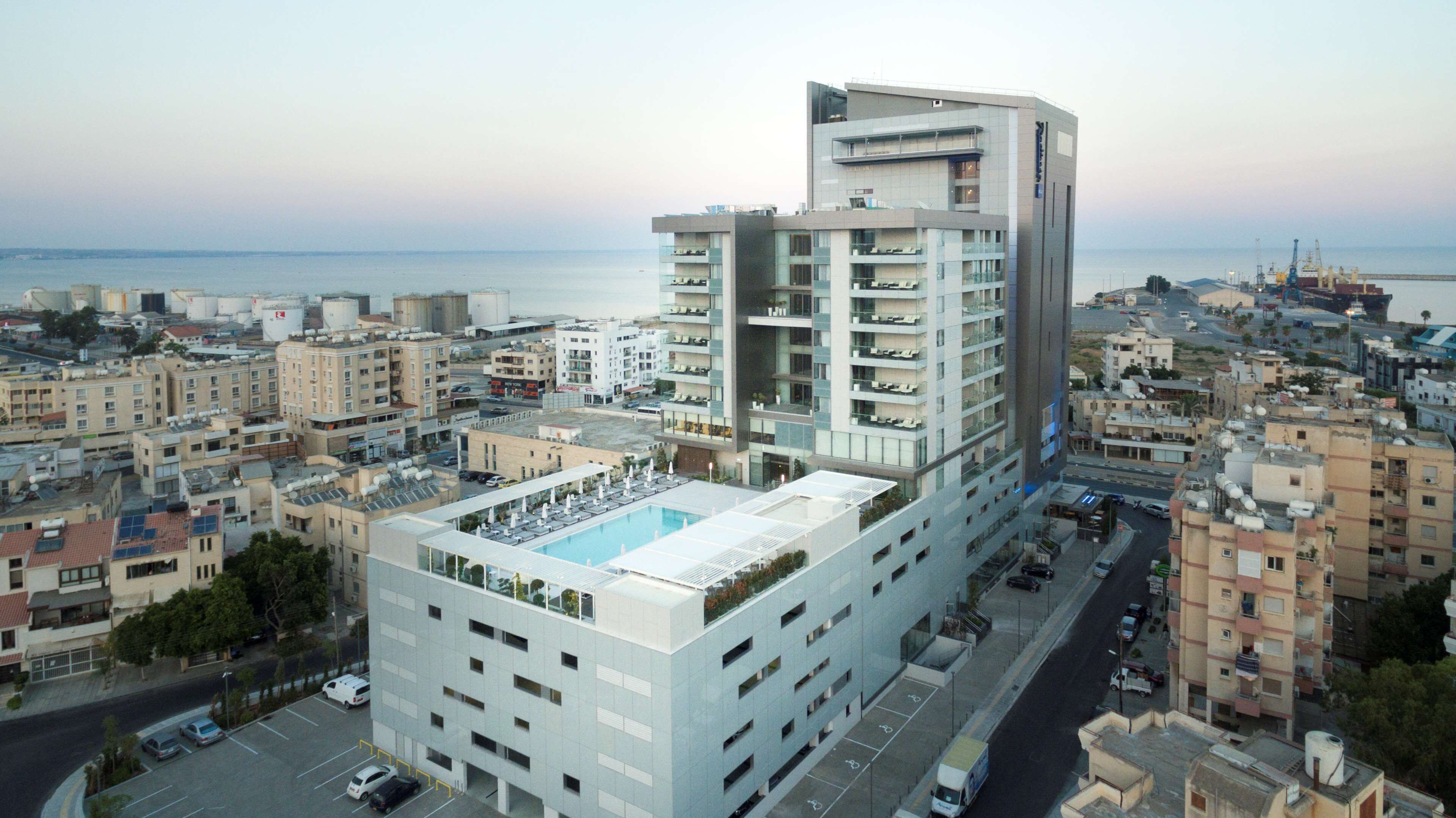Un moderno hotel de gran altura con varios pisos, una piscina en la azotea y vista al mar.