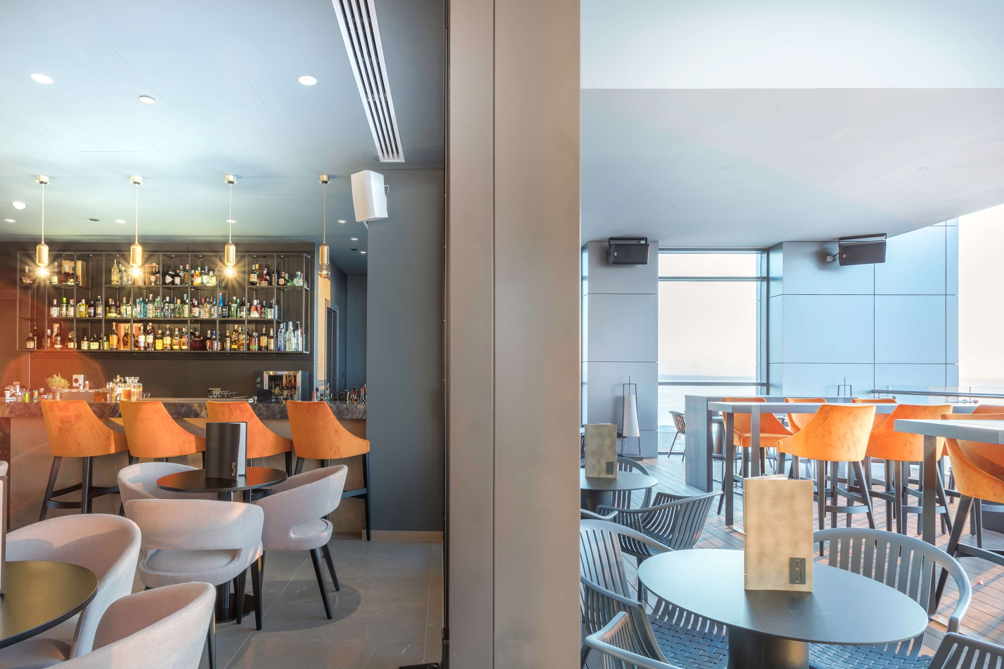 A modern bar area with a variety of liquor bottles and a seating area with orange chairs and tables.