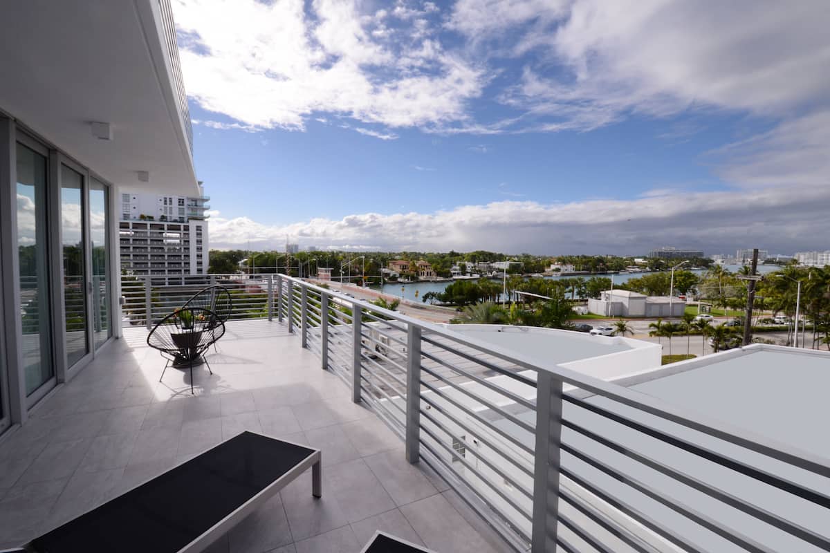 Un balcón moderno con vistas a un paisaje urbano, un comedor con mesa y sillas, y una piscina al fondo.