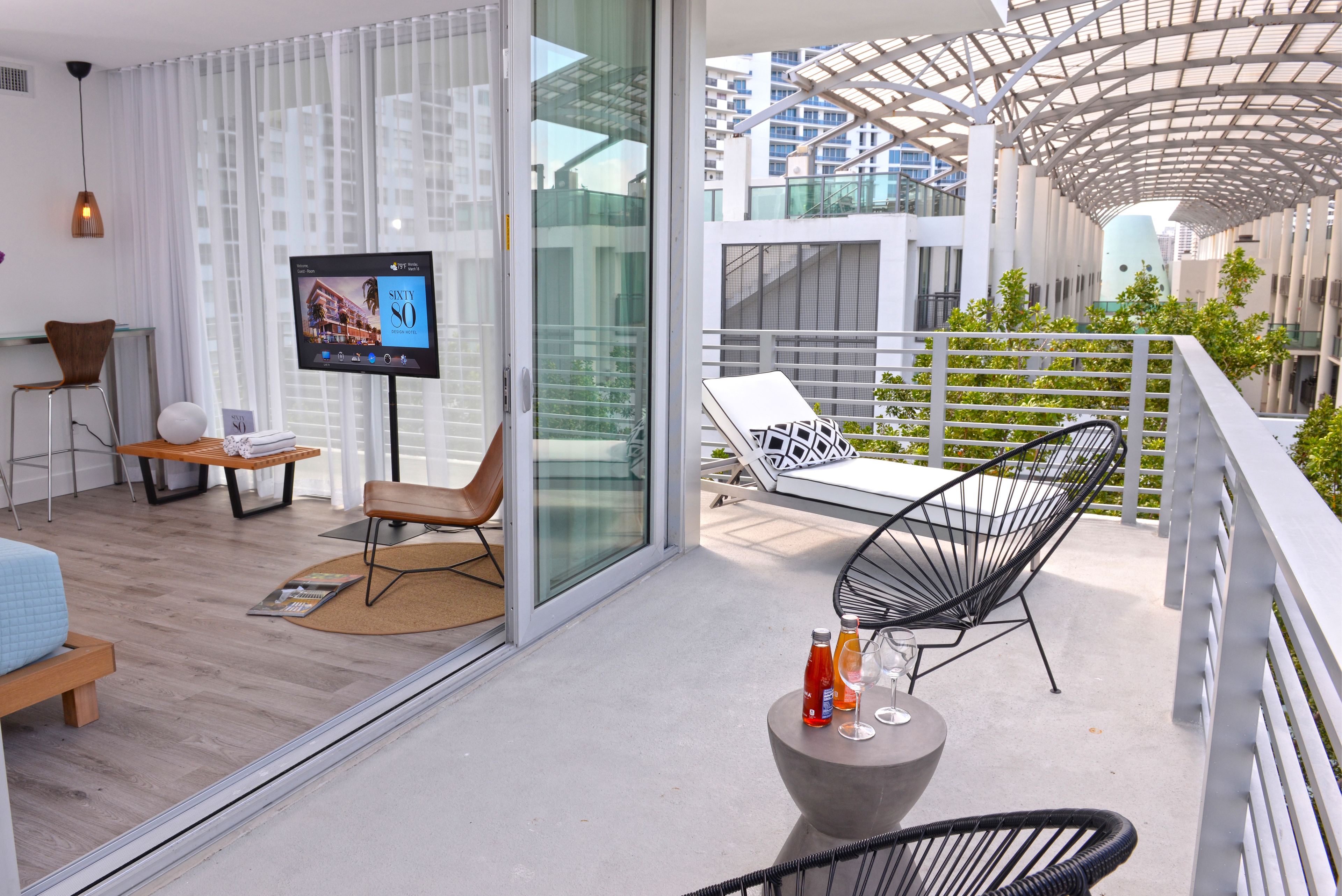 A modern hotel balcony with a TV, seating, and a view of the city.