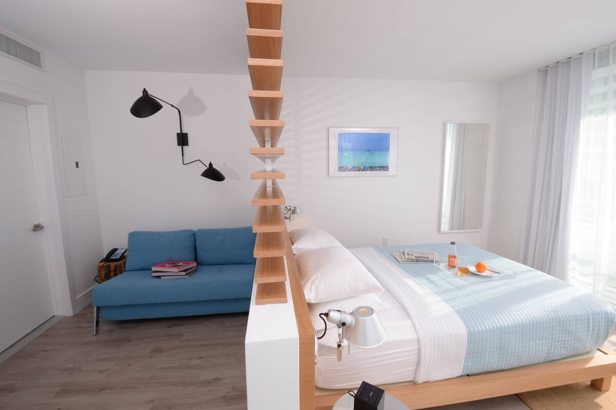 Un dormitorio con una cama, un sofá azul, una estructura de escalera de madera, un escritorio y una lámpara.