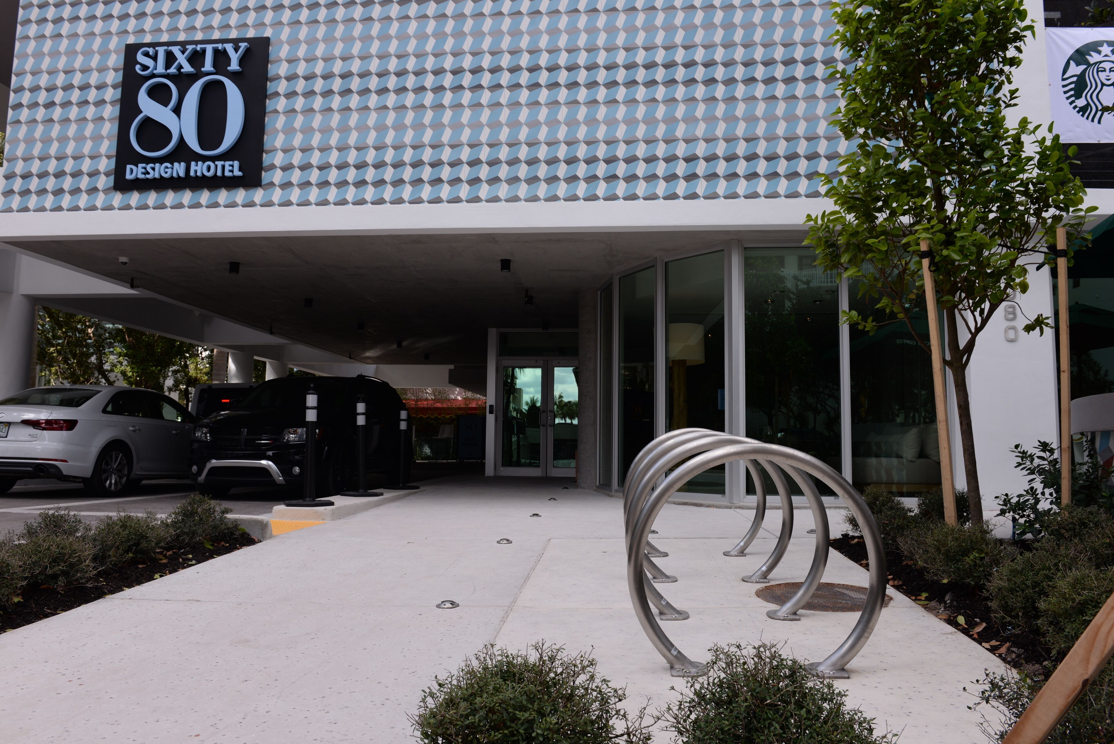 The entrance of the Sixty 80 Design Hotel with a modern geometric facade, a parking area, and a metal sculpture.