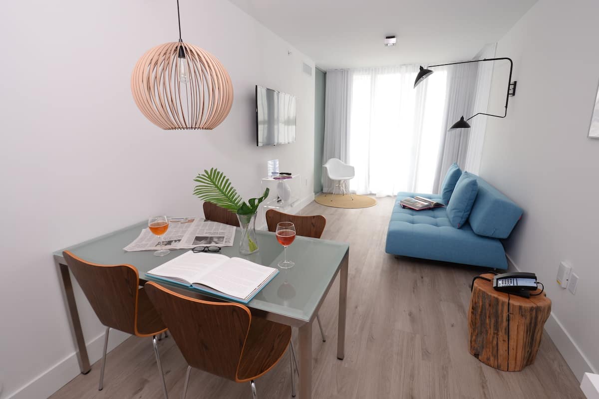 Una sala de estar moderna con comedor, que presenta un sofá azul, sillas de madera, una mesa de vidrio y una mesita de madera con un teléfono.