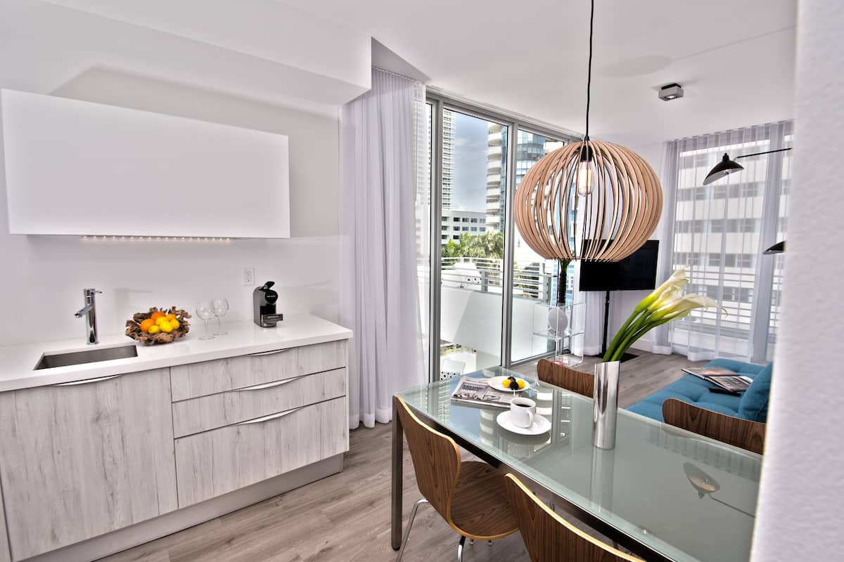 Una cocina moderna con una mesa de comedor de vidrio, armarios blancos y vistas de la ciudad a través de grandes ventanales.