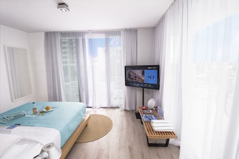 A modern hotel room with a large TV, a balcony with a view of the city, and a bed with a blue cover. at 6080 Design Hotel by Eskape Collection