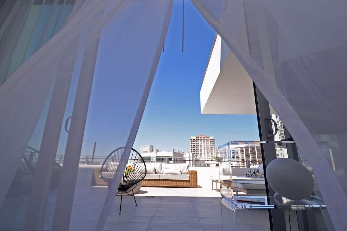 Una terraza moderna en la azotea con un sofá blanco, una silla de mimbre y una mesa de vidrio.