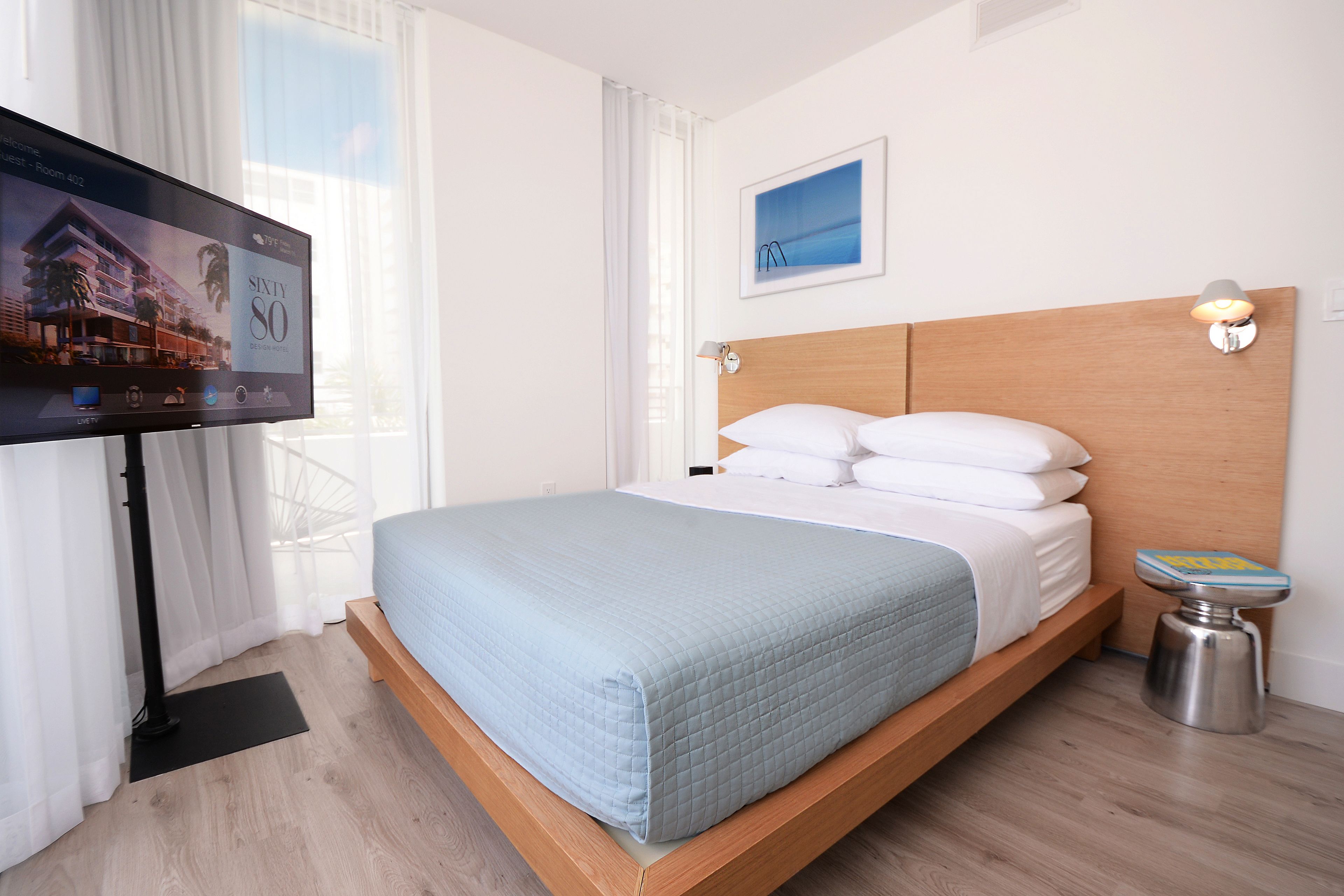Une chambre d’hôtel moderne équipée d’un lit, d’une télévision, d’une table de chevet et d’une fenêtre avec des rideaux.