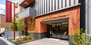 Fachada de hotel en rojo y gris, con un letrero y un pequeño jardín.