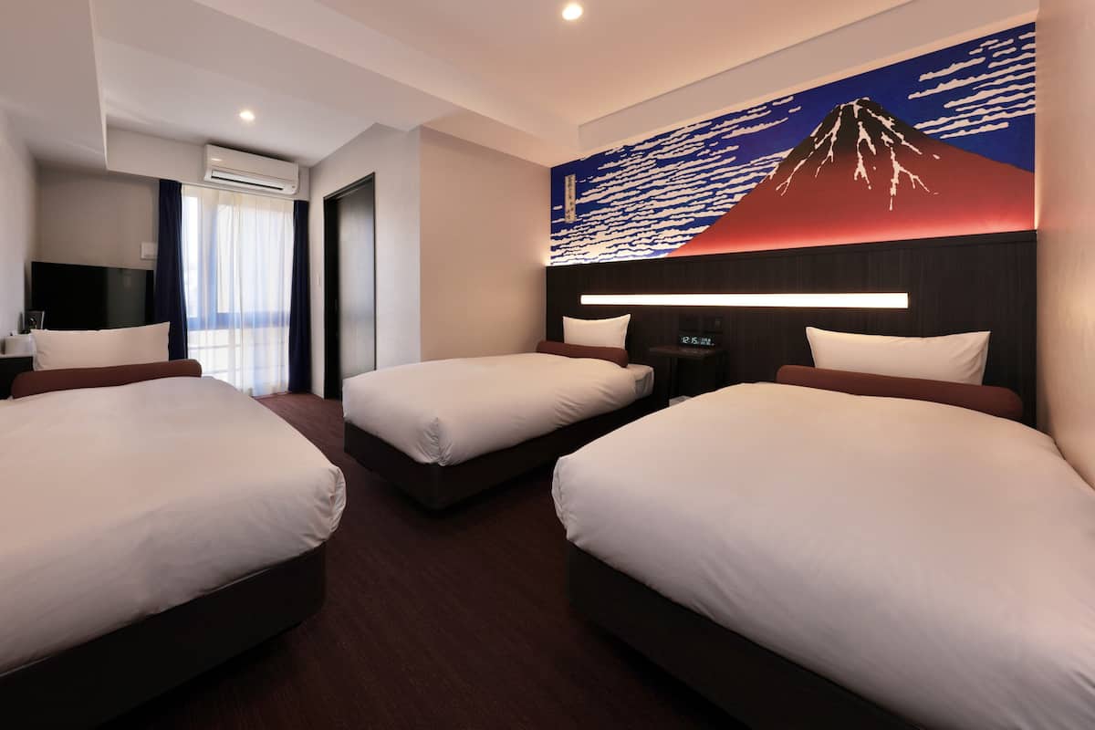A hotel room with three single beds, a large wall mural, a flat-screen TV, and a bedside table with a clock.