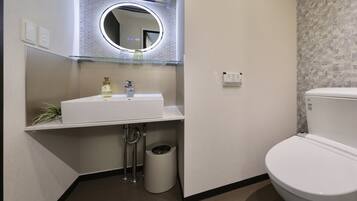 A bathroom with a white sink, a mirror, a toilet, and a trash can.