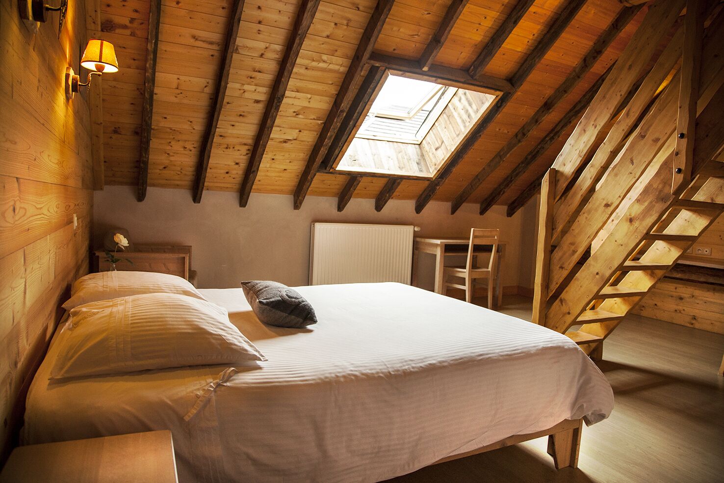 A bedroom with a sloped ceiling, a skylight, a bed with pillows, a nightstand, and a chair.