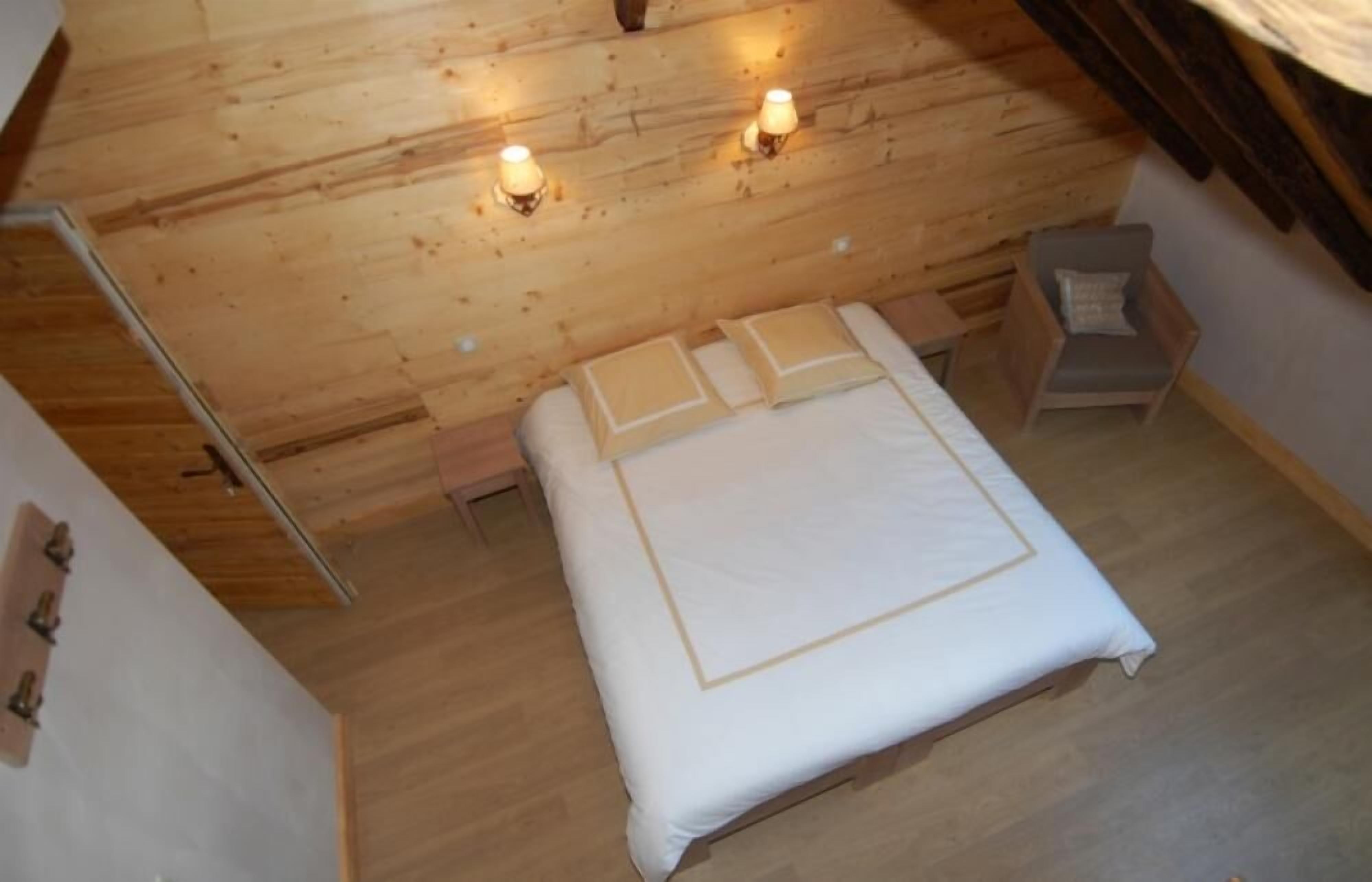 Une chambre avec un plafond en bois, un lit avec une literie blanche, deux lampes de chevet et une petite chaise avec un coussin.