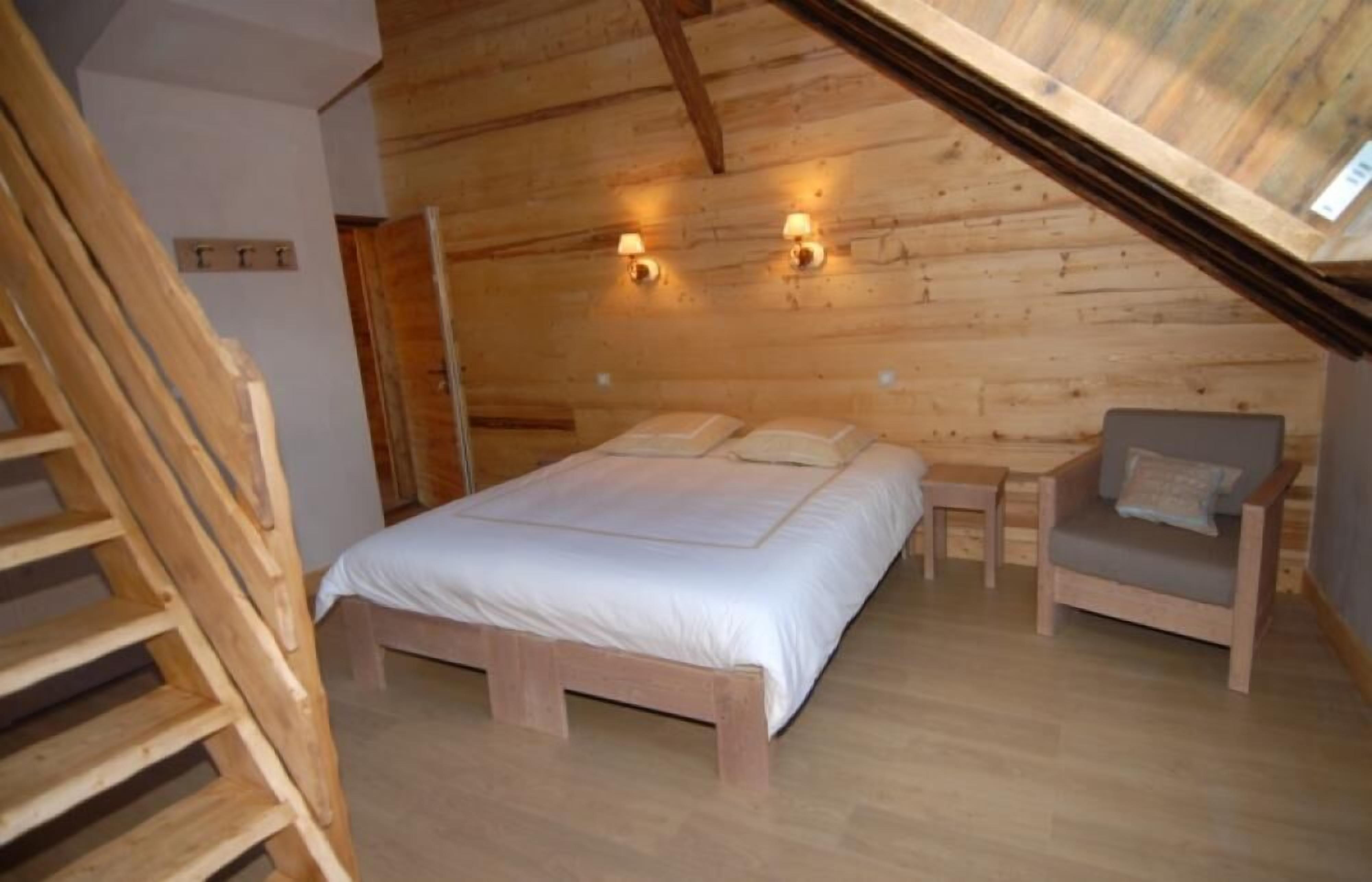 A wooden bedroom with a bed, bedside tables, and a chair.