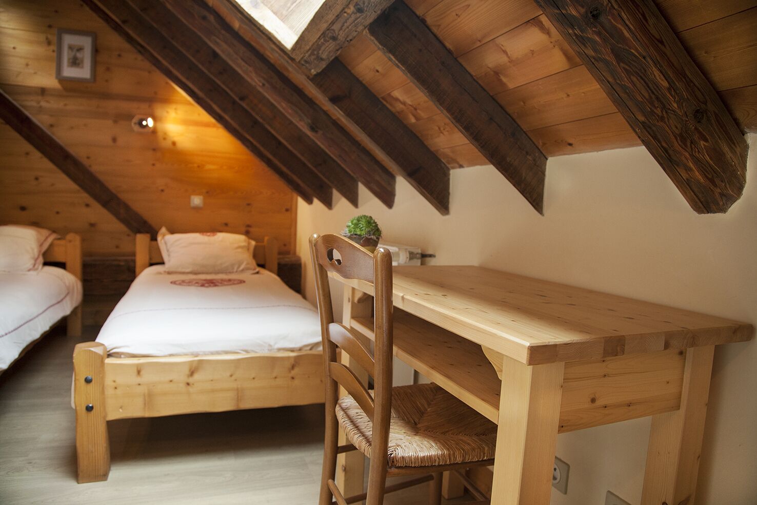 Un dormitorio acogedor en el ático con una cama litera de madera, un escritorio de madera con una silla y una pequeña planta en maceta.