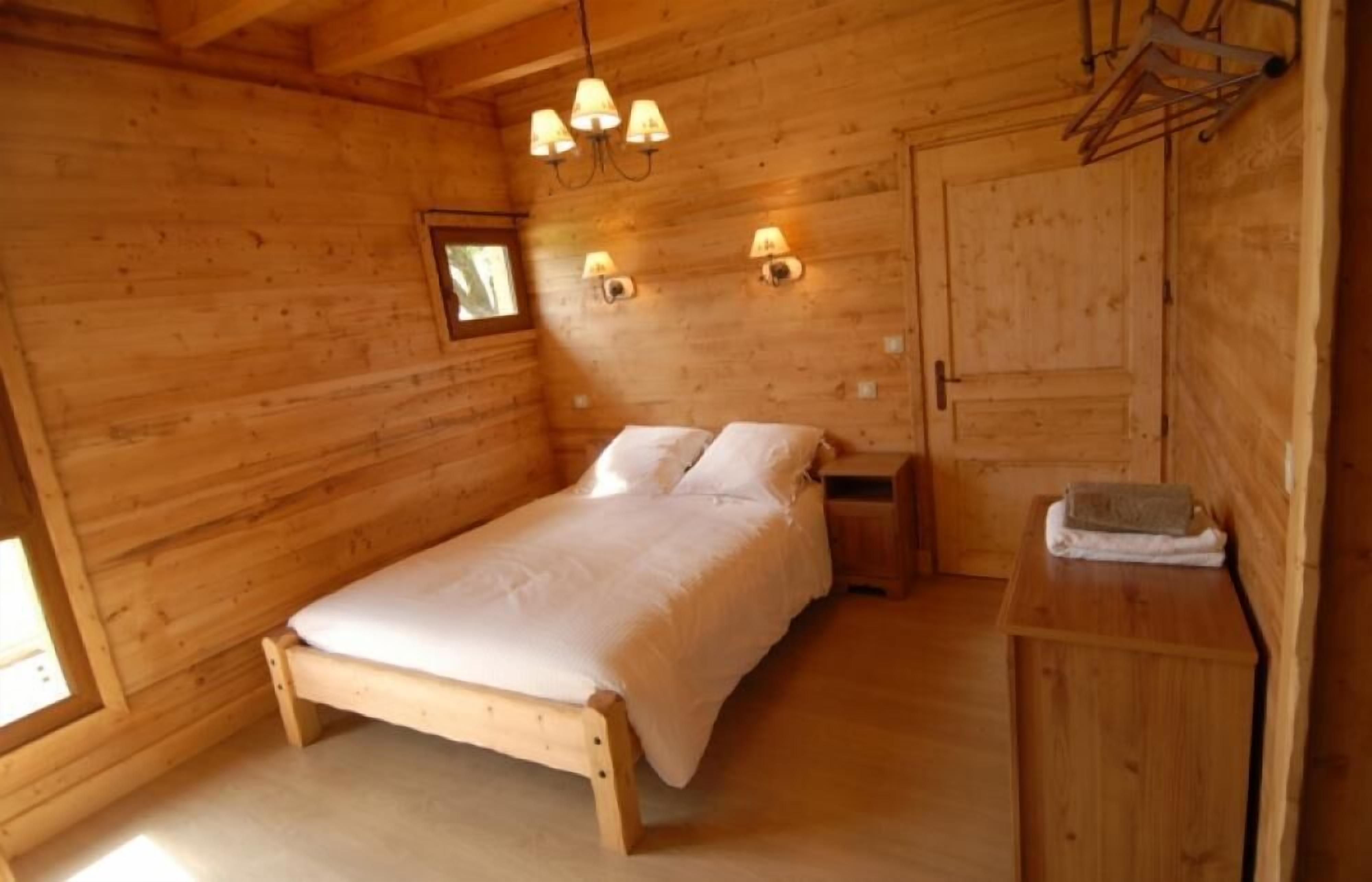 Une chambre dans un chalet en bois, avec un lit, des tables de chevet et des lampes fixées au mur.