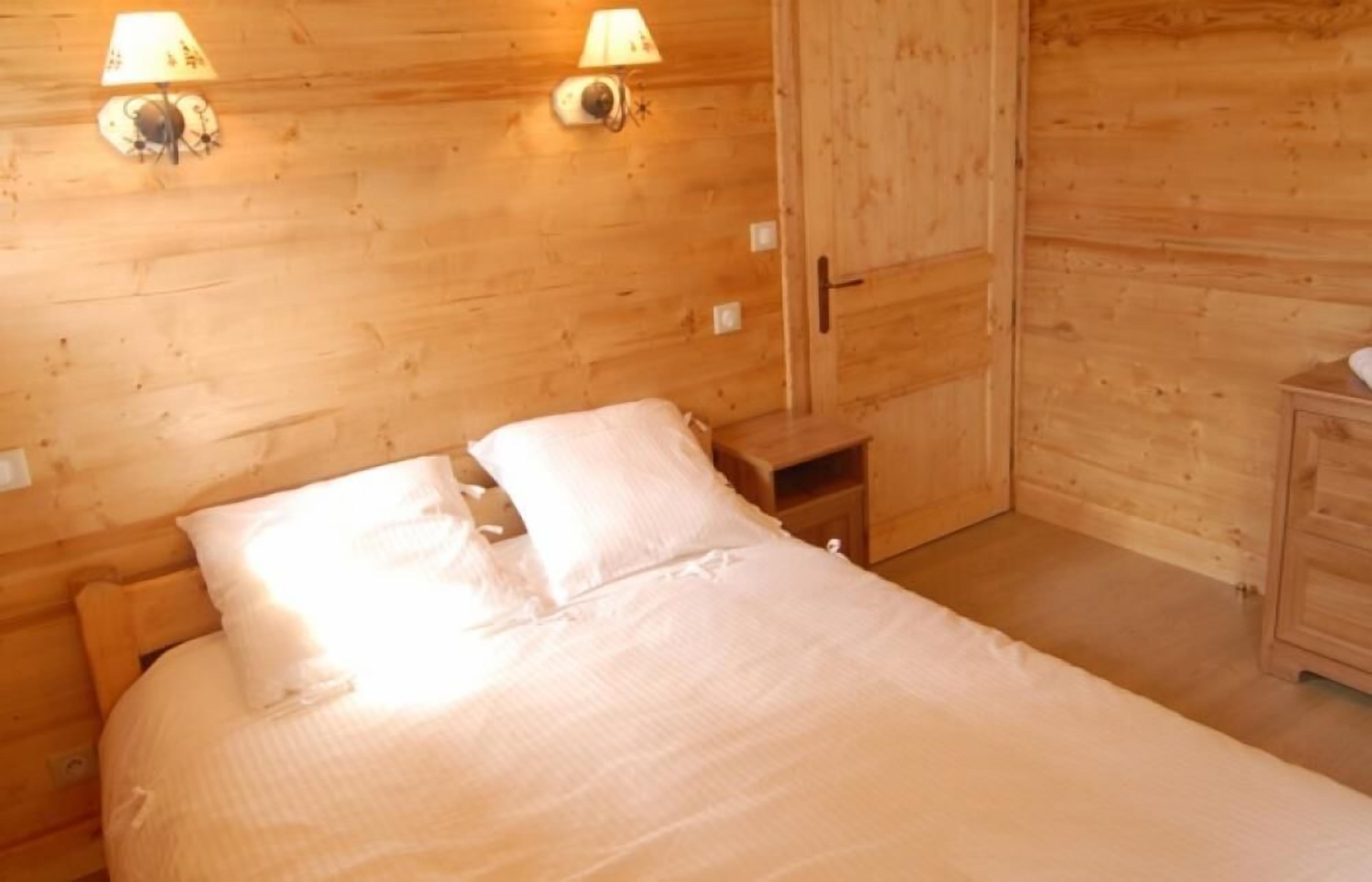 Une pièce en bois avec un lit, deux lampes fixées au mur et une armoire en bois.