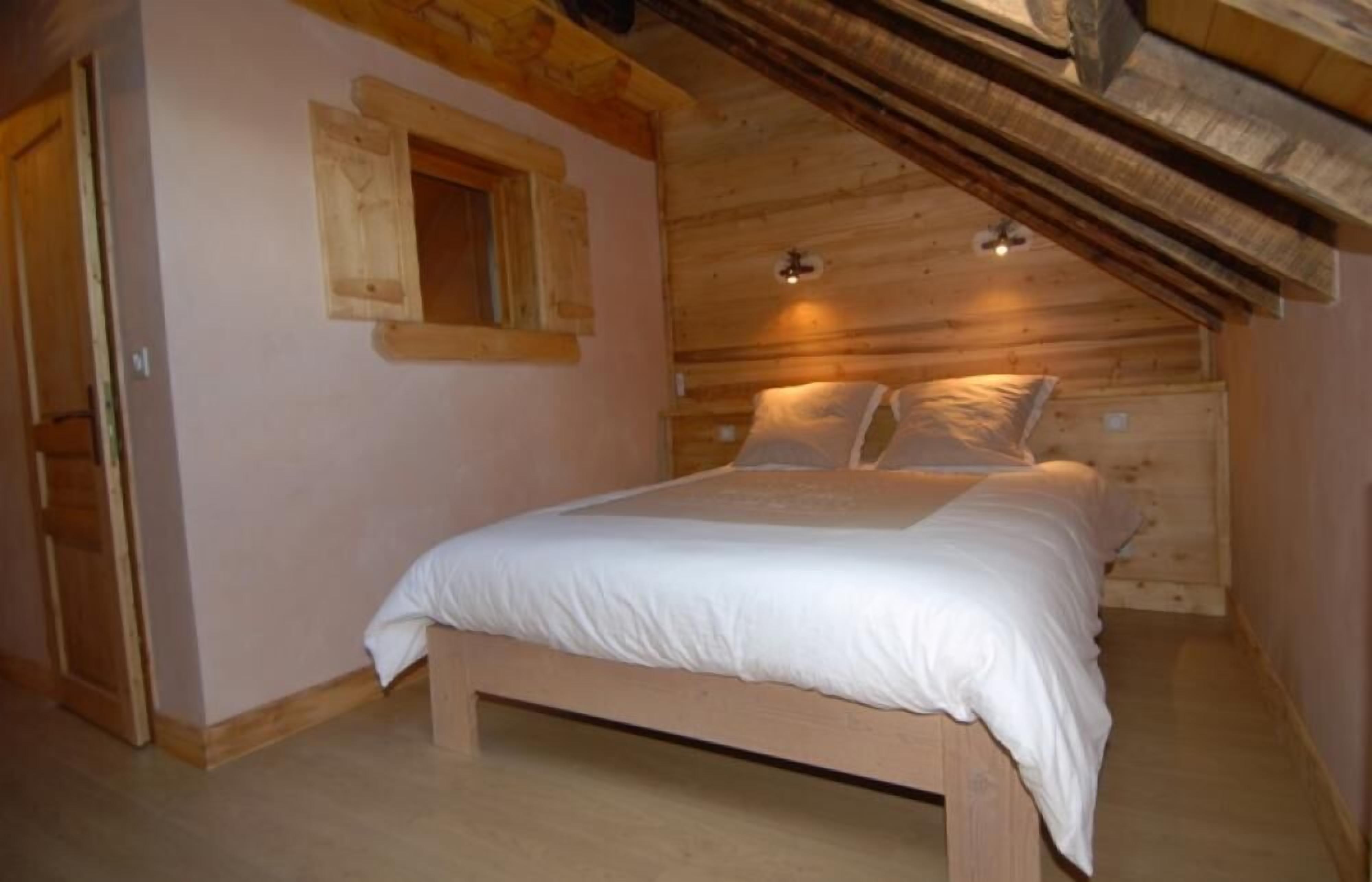 A wooden room with a bed, a window, and a sloped ceiling.