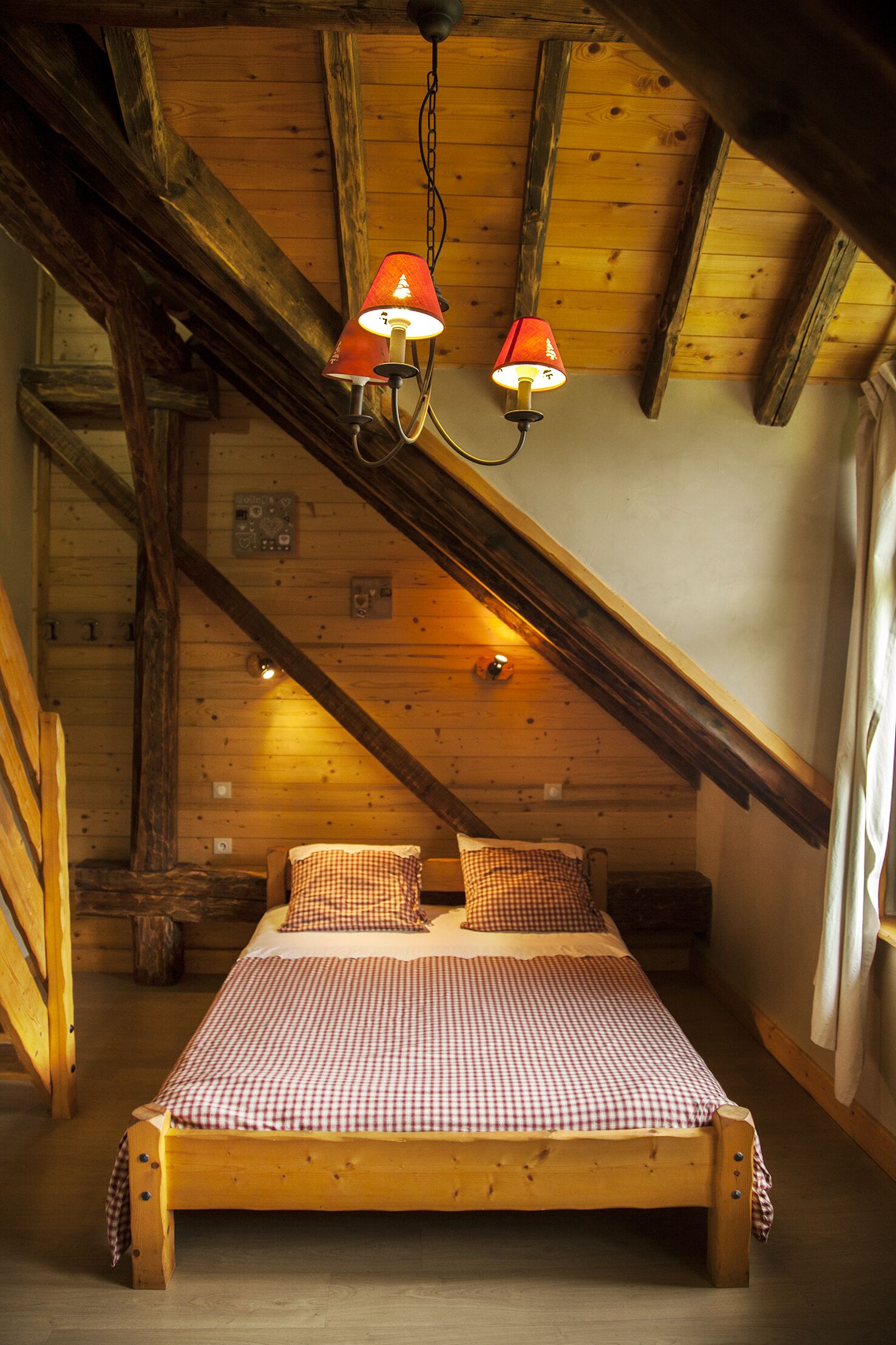 Un lit en bois avec une literie à carreaux, dans une pièce dont on peut voir les poutres apparentes et qui possède un plafond en pente.