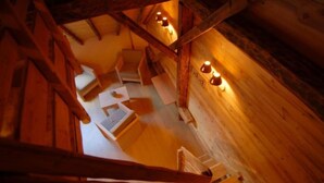 Un intérieur en bois avec un plafond en pente et des poutres apparentes. On y trouve deux appliques murales et une petite table avec une chaise.