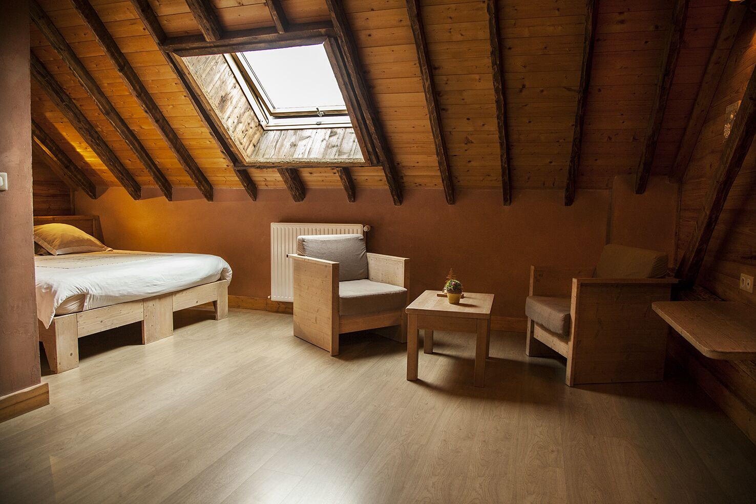 A cozy attic bedroom with a skylight, a bed, a chair, a small table, and a radiator.