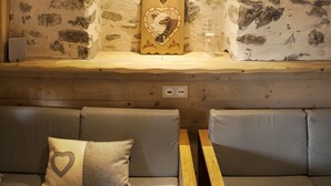 Une pièce chaleureuse avec un mur en pierre, un banc en bois et un banc rembourré agrémenté d’un coussin en forme de cœur.