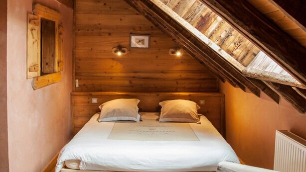 Une chambre mansardée chaleureuse, avec un lit en bois, une petite chaise et une lucarne.