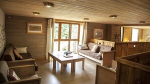 L’intérieur d’un chalet en bois chaleureux et accueillant, avec un canapé, des fauteuils, une table et un coin cuisine.