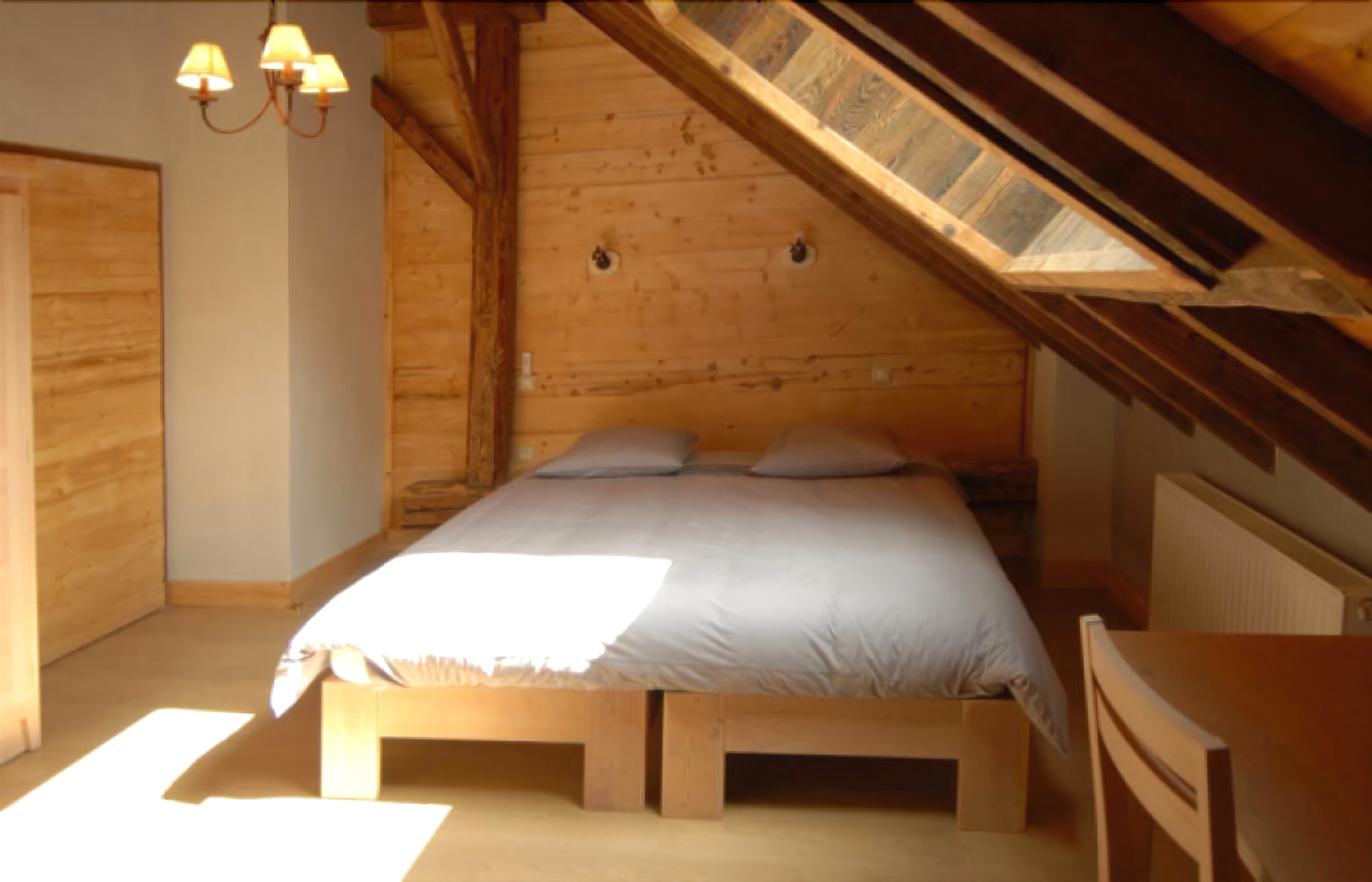 A wooden bedroom with a sloped ceiling, a bed with pillows, and a small wooden bench.