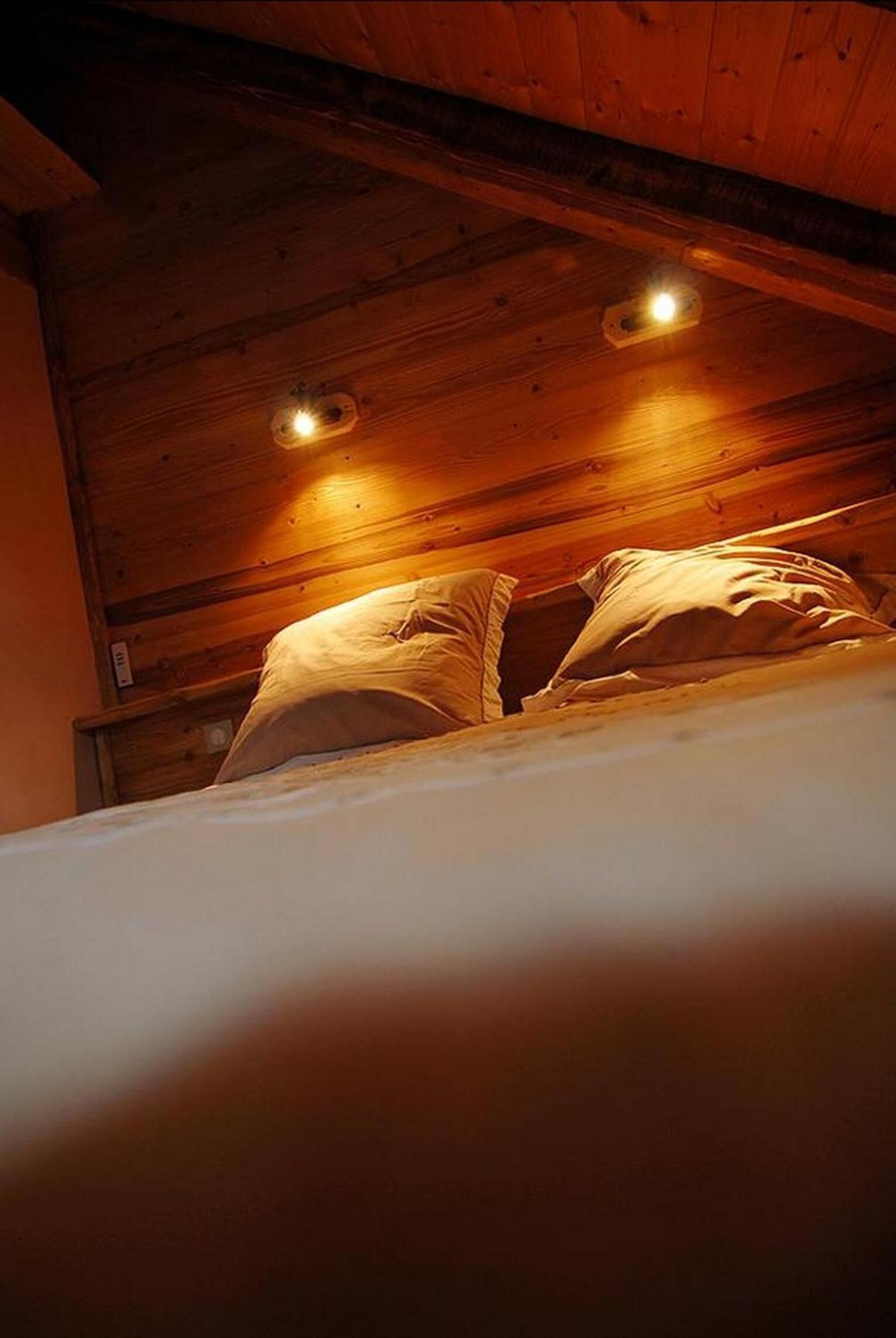 A wooden ceiling with recessed lighting and a bed with pillows.
