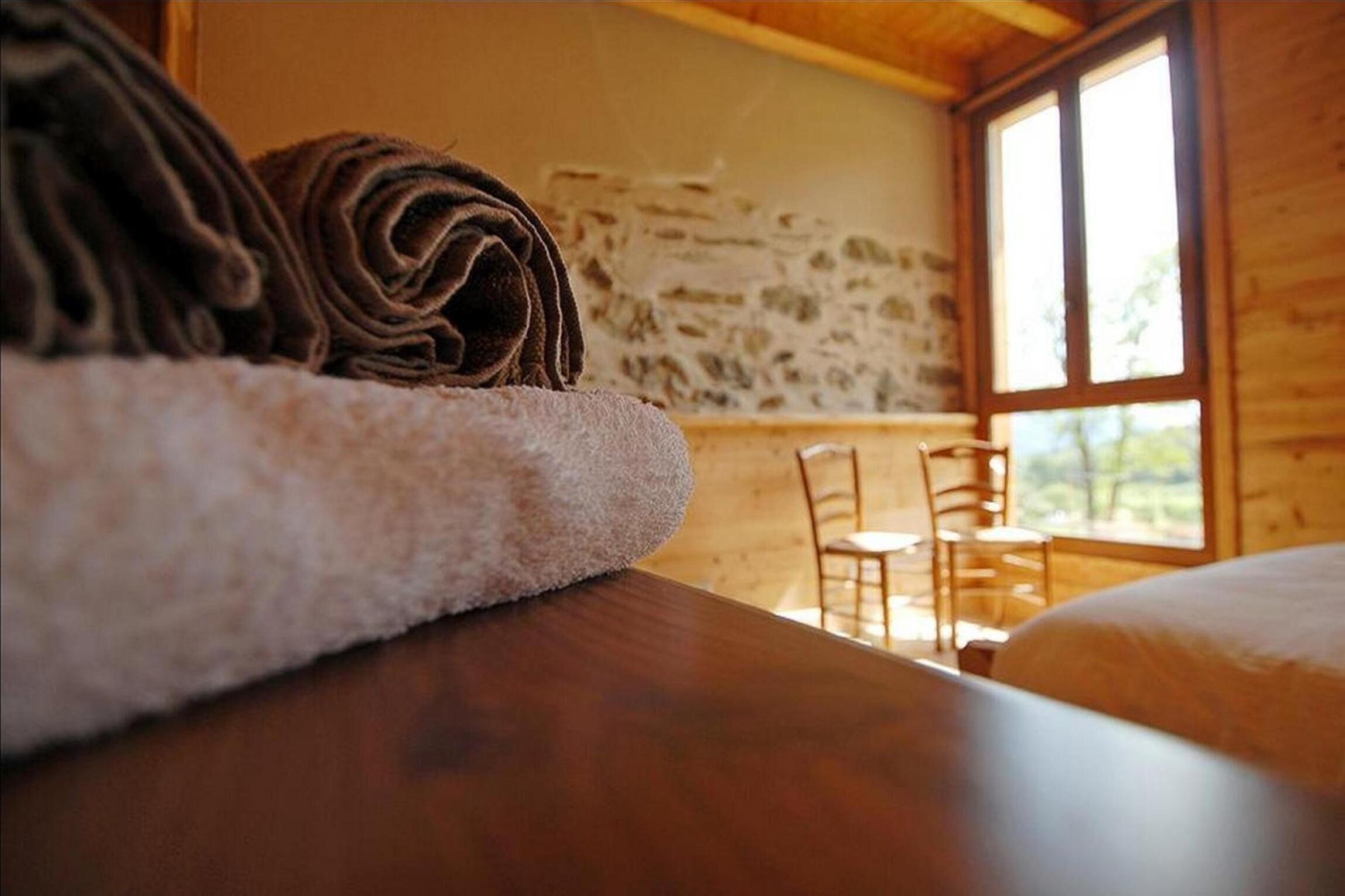 Une pièce chaleureuse avec une table en bois, une serviette enroulée et une vue sur un mur de pierre et une fenêtre.