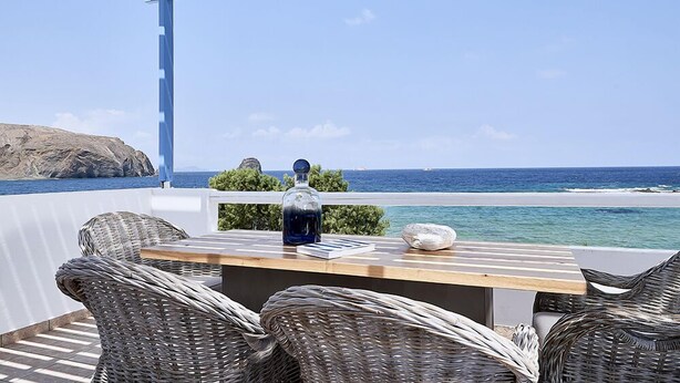 A terrace with wicker furniture, a wooden table, and a view of the ocean. - Villa Delmar - Delmar Collection (Milos)