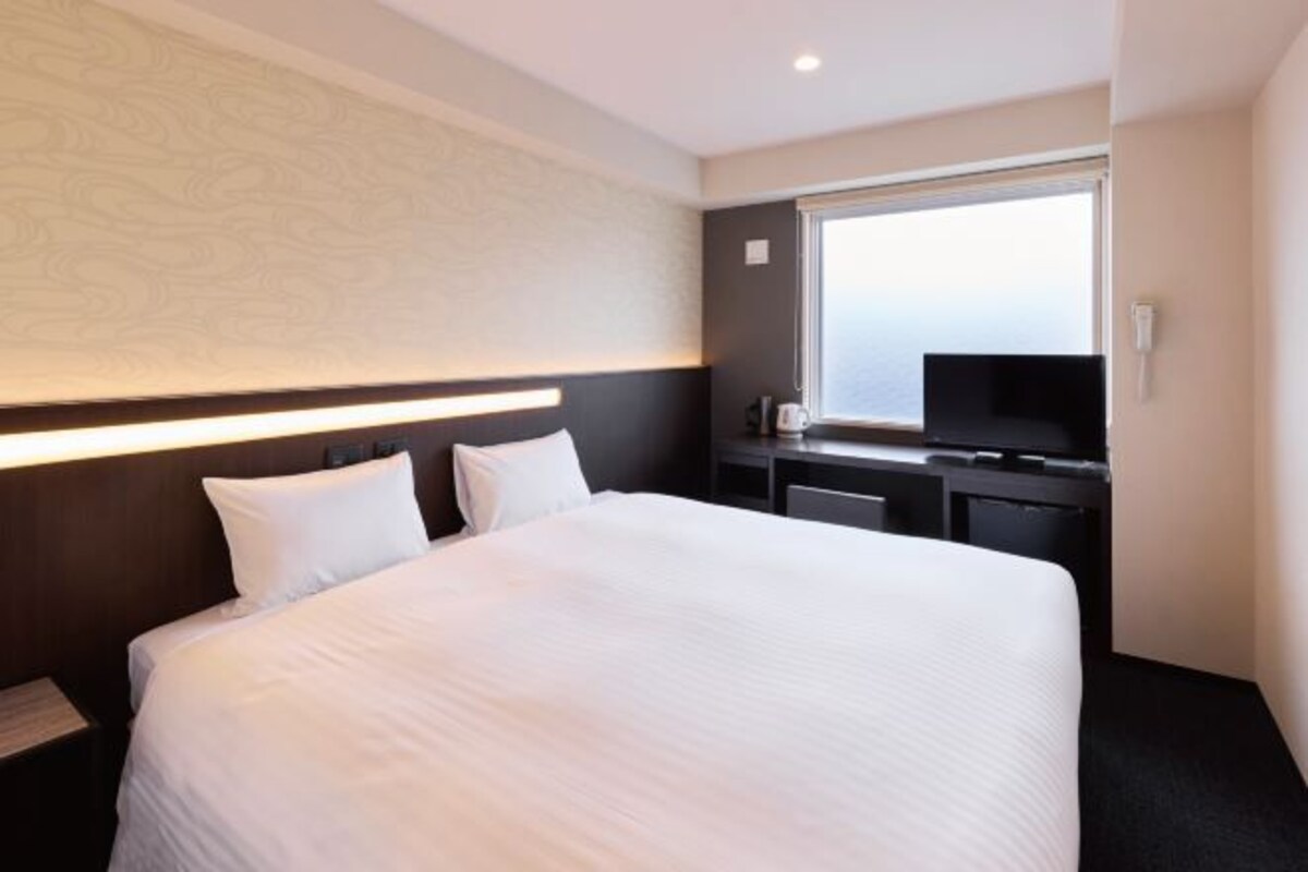 A hotel room with a large bed, a desk with a TV, and a window.