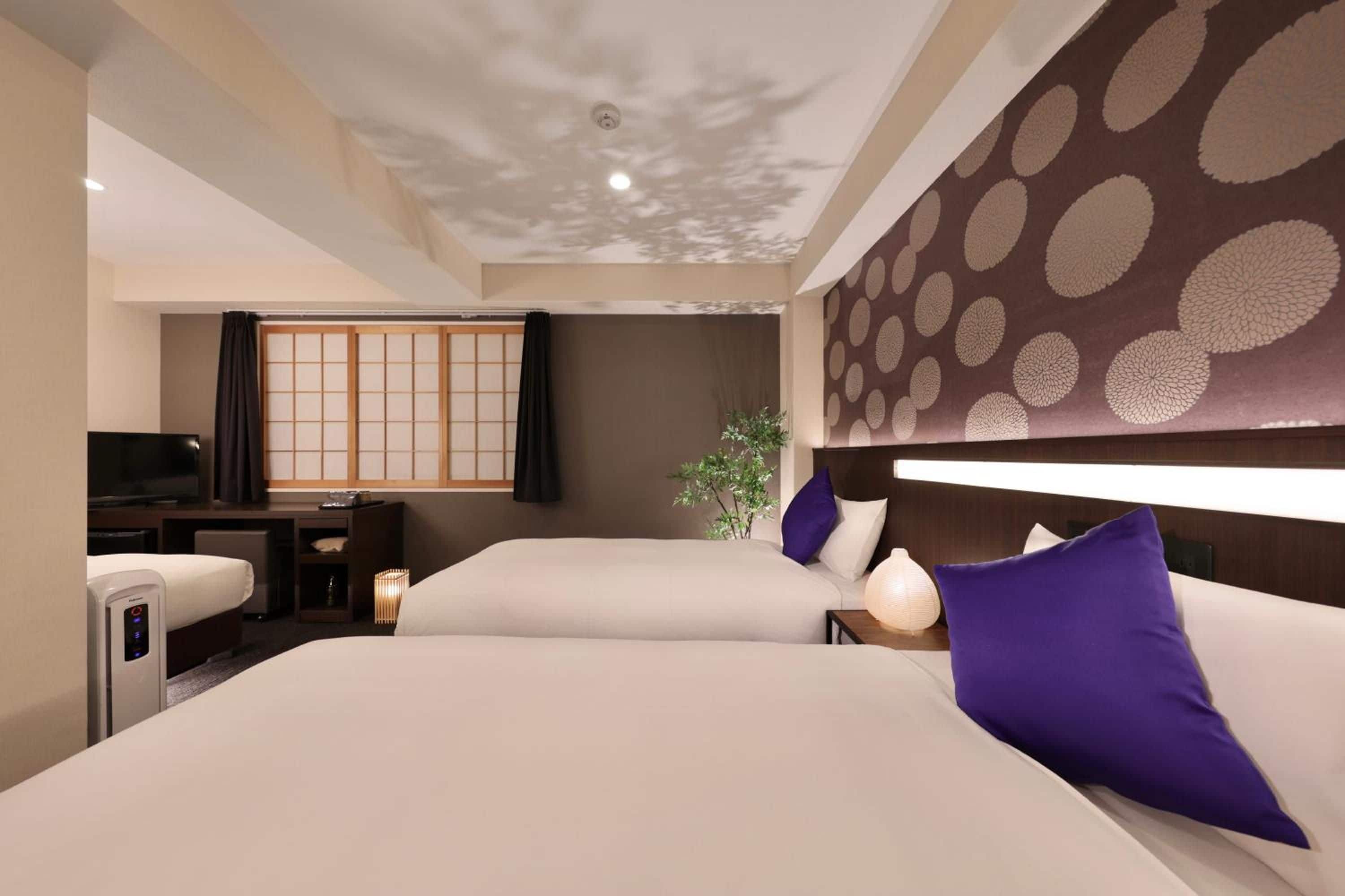 A hotel room with two beds, a television, a desk, and a traditional Japanese sliding door.