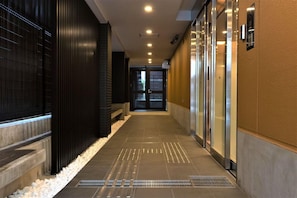 A corridor with a tiled floor, a metal grate, and a door at the end. - MARUTAMACHI Crystal Hotel (Kyoto)