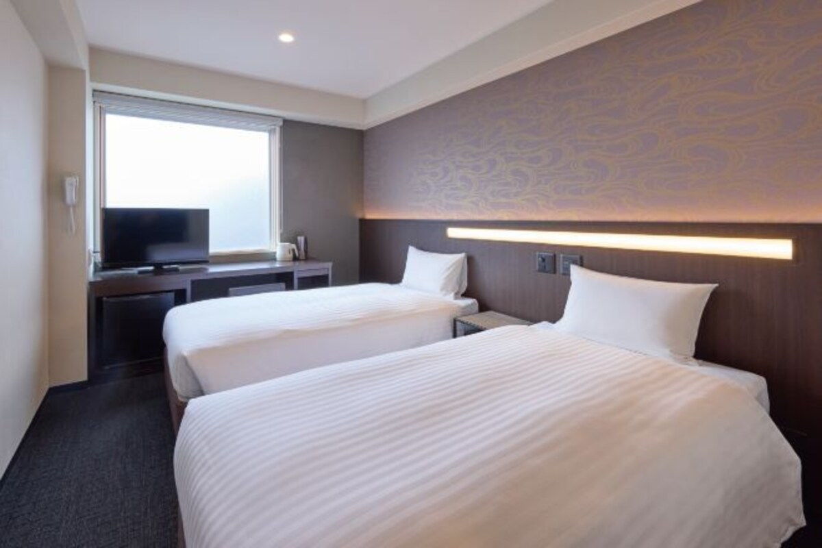 A hotel room with two beds, a TV, a desk, and a large window.
