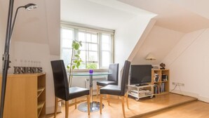 Uma sala de estar moderna com uma mesa de jantar de vidro, cadeiras pretas, uma televisão e uma estante de livros.