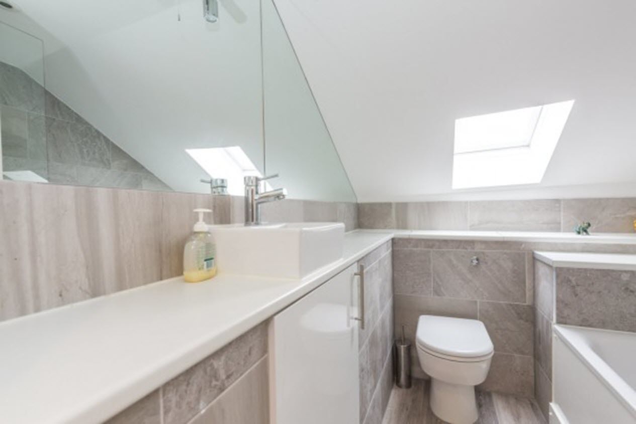 A modern bathroom with a skylight, a sink, a toilet, and a mirror.