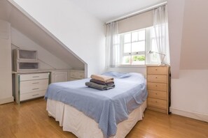 A bedroom with a bed, a desk, and a window.