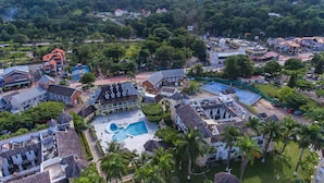 Vista aèria d'un complex turístic amb una piscina, diversos edificis i vegetació exuberant.