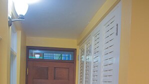 Un passadís amb una porta de fusta, un paviment de rajola i un armari blanc amb portes a persianes.
