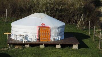 Una yurta con plataforma de madera y una puerta central, rodeada de un área cubierta de césped y árboles.