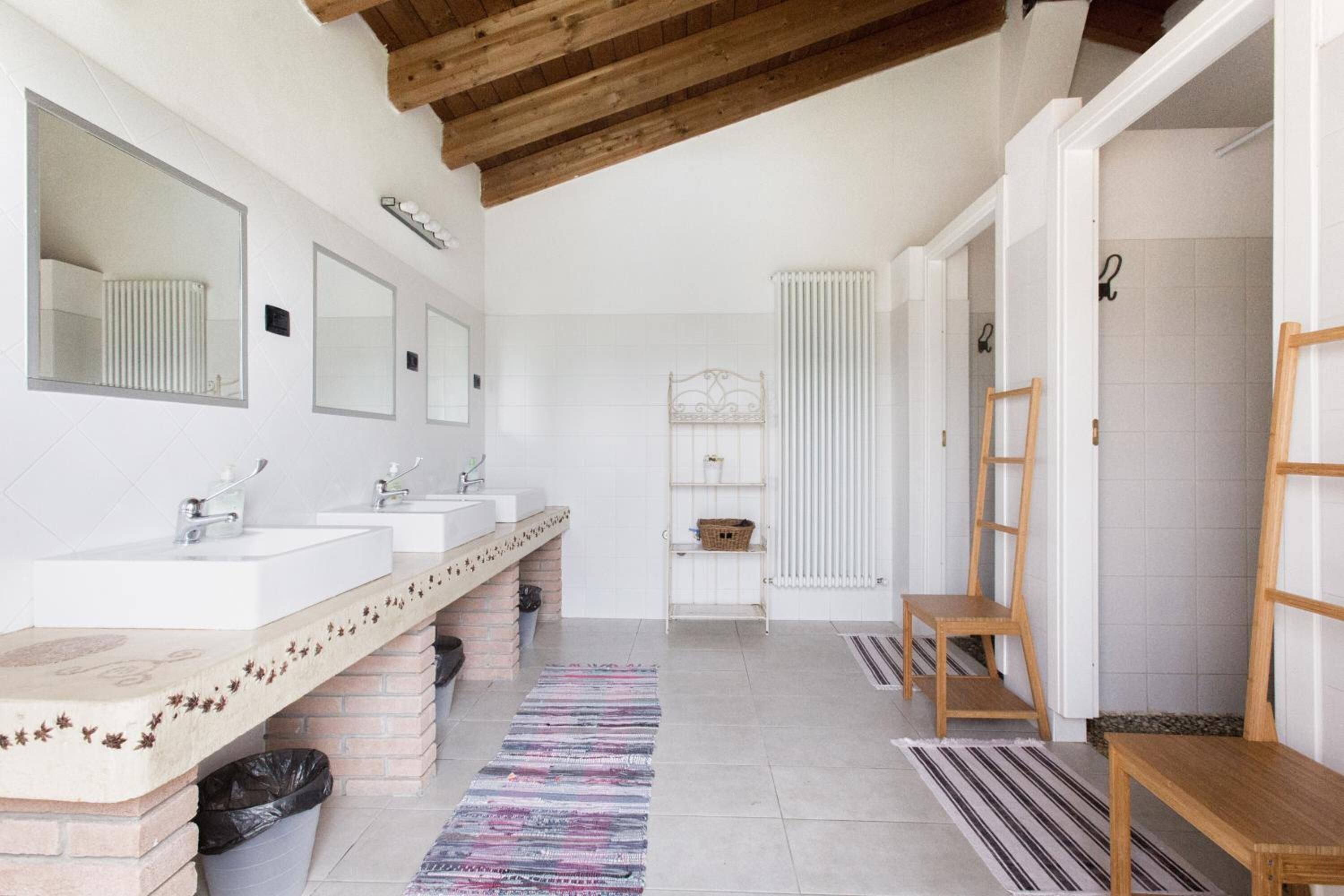 Un baño moderno con tres lavamanos, un espejo grande, un radiador y un banco de madera.